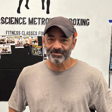 Man in workout clothes posing at a boxing gym with jump ropes in the background.
