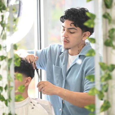Barber carefully cutting client's hair in a bright, plant-filled salon.