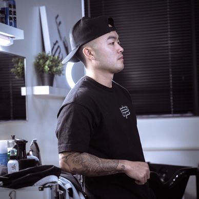 Man with tattoos wearing a black cap and shirt in a modern room.