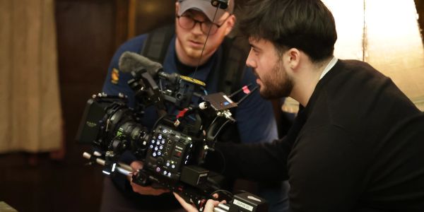 Two men operating a professional video camera indoors.
