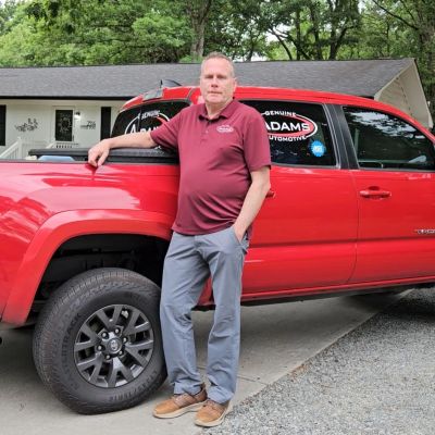 Man leaning on a red pickup truck.