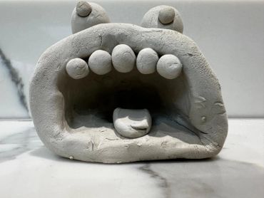 A clay sculpture resembling a wide-mouthed creature with eyes and teeth.