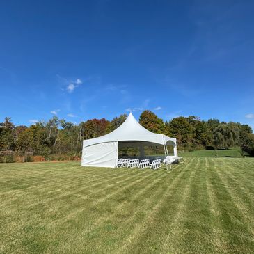 White event tent with chairs on a large green lawn under a clear blue sky.