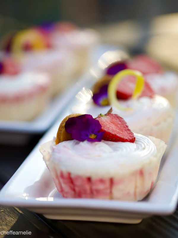 Petits gâteaux au fromage individuels, décorés de fraises fraîches, de zeste de citron et de fleurs