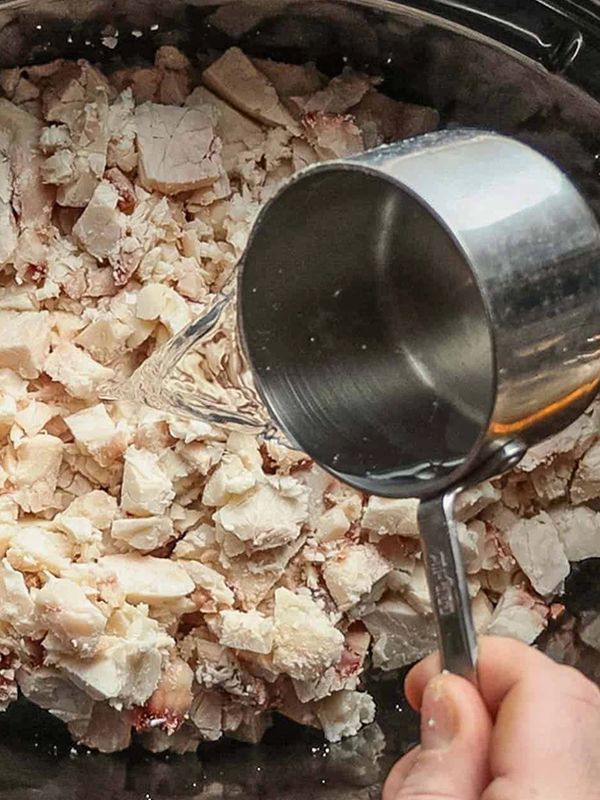 Pouring liquid into chopped cooked chicken in a bowl.