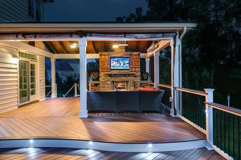Covered deck with stone fireplace and outdoor television glowing at night