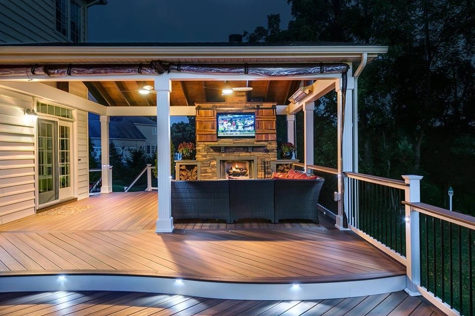 Covered deck with stone fireplace and outdoor television glowing at night