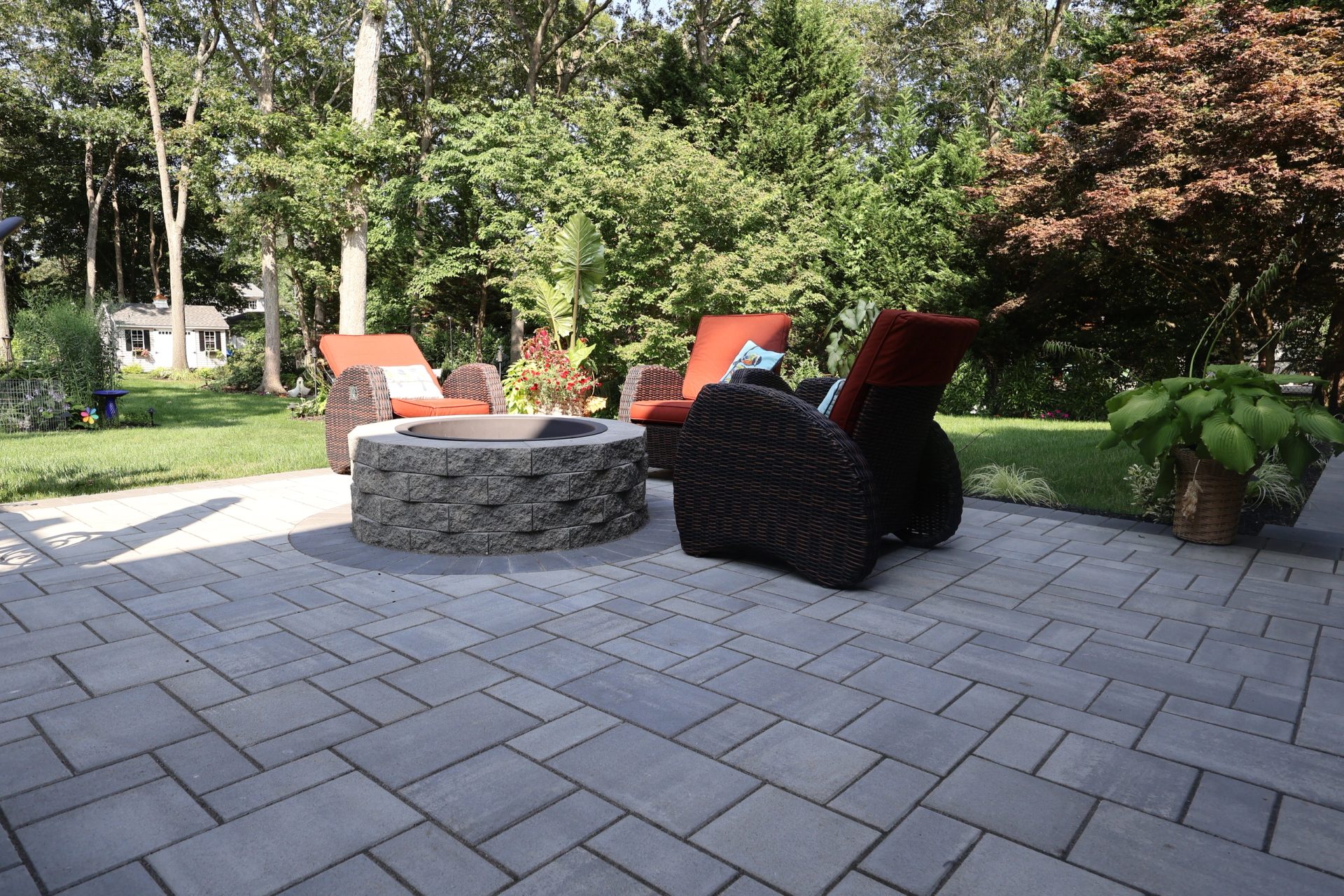 Round stone fire pit with lounge chairs on a paver patio