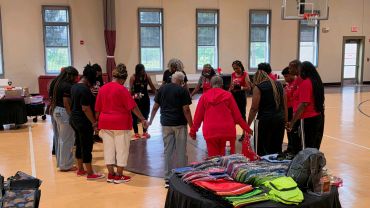 Group of women standing in a gymnasium holding hands in a circle.