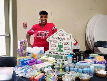 Person smiling behind a table with many hygiene products.