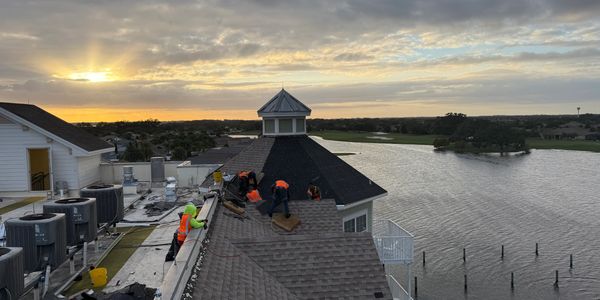 Roofing crew at dusk. Roofers on hotel. Large shingle roof.