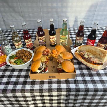 Variety of sandwiches, bowls, and soda bottles on a checkered tablecloth.