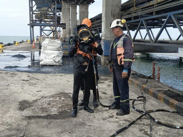 Dos trabajadores con equipo de buceo en un muelle industrial.