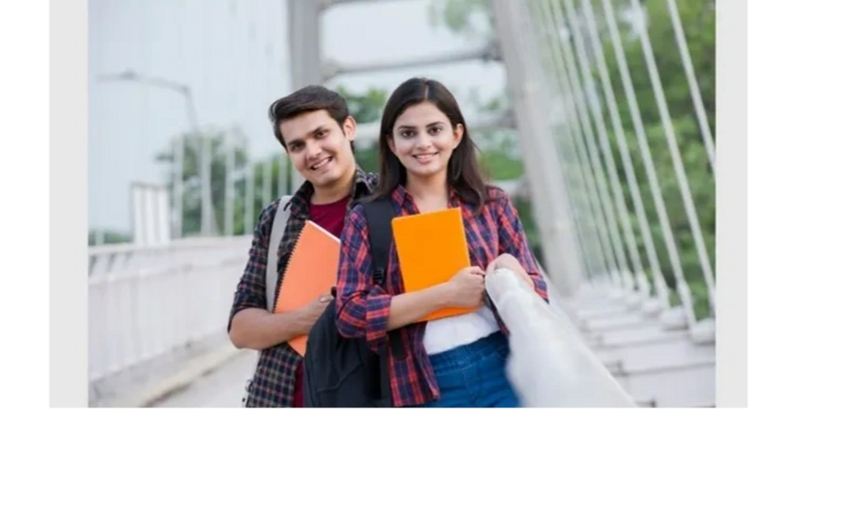 Two smiling students holding orange notebooks on a bridge outdoors.