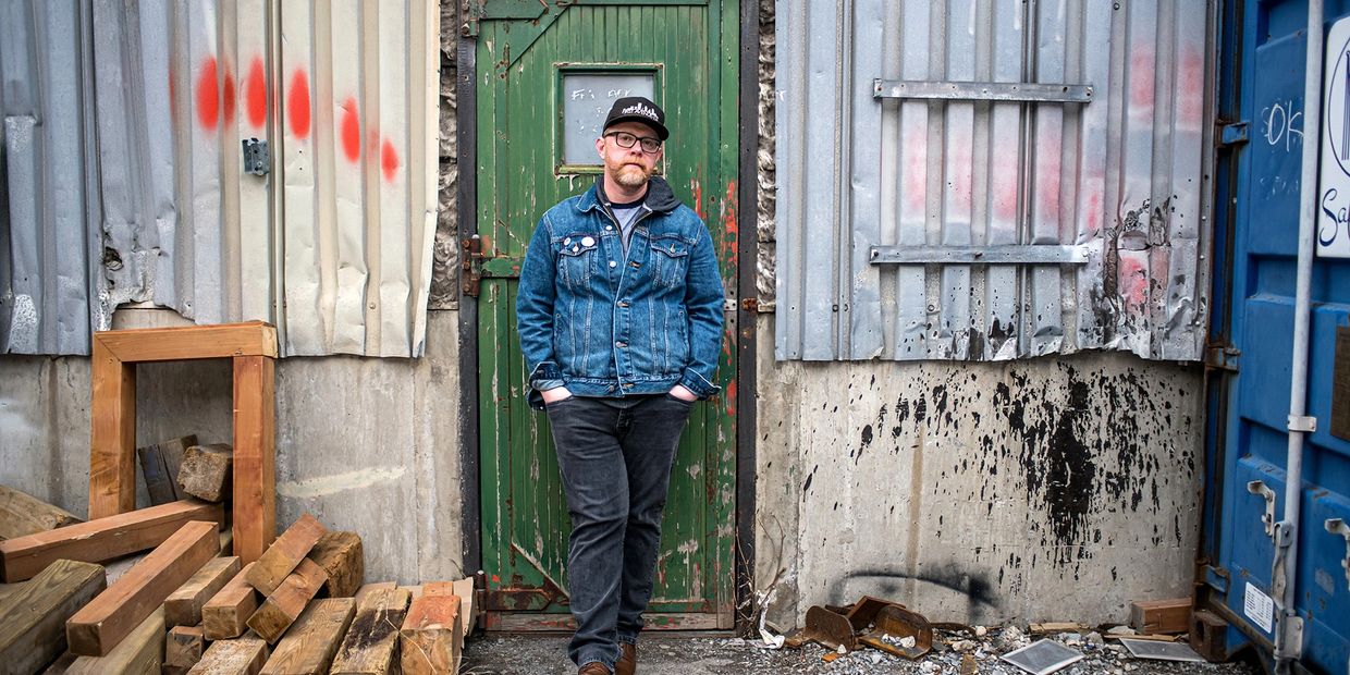 Man in denim jacket standing in front of a weathered green door.