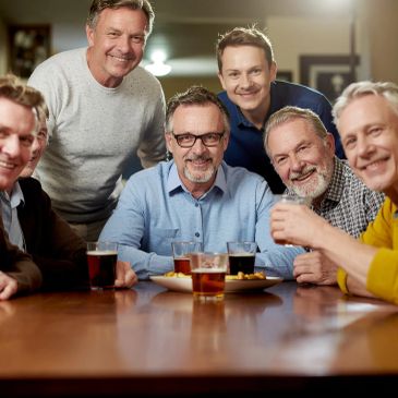 Group of six men smiling with drinks at a table.