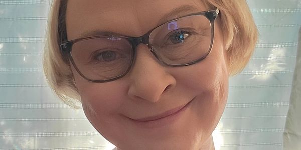 Smiling woman with glasses and short blonde hair in soft natural light.