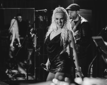 Energetic female singer performing on stage with band in black and white.