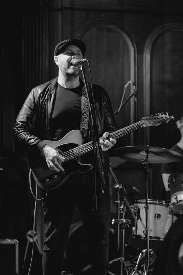 Black and white photo of a musician singing and playing guitar on stage.