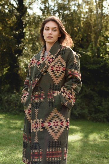 Woman wearing a patterned long coat outdoors in a natural setting.
