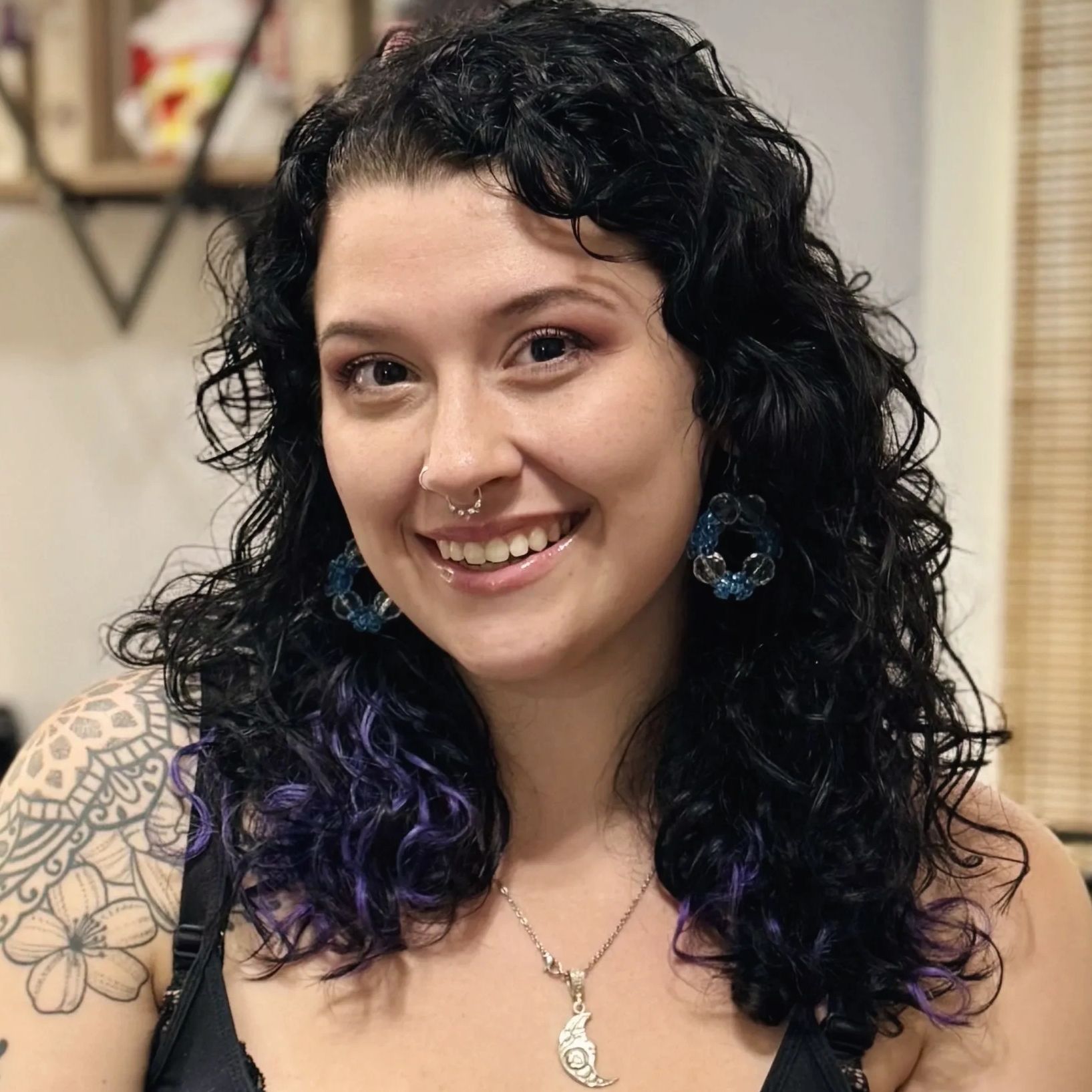 A headshot of a white woman with curly black and purple hair sitting in her salon chair.