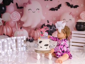 Baby in Halloween-themed photoshoot with cake and decorations.