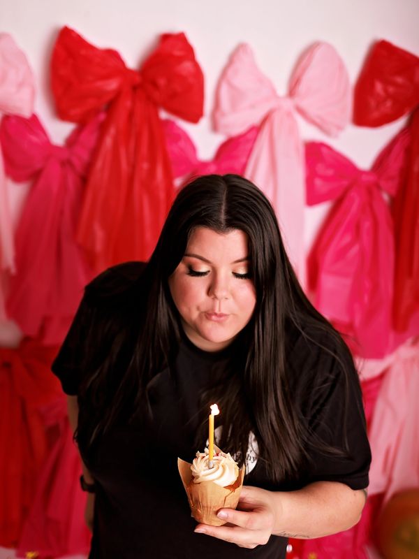 Woman blowing out a candle on a cupcake with colorful bows in the background.