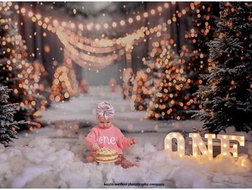 Baby girl celebrating first birthday with cake and lights.