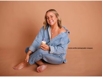 Woman in denim outfit holding a cupcake with a candle.