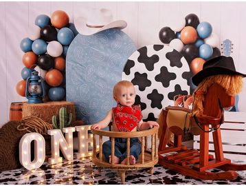 Baby in cowboy-themed photo setup with balloons and decorations.