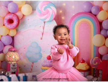Happy toddler in pink sweater clapping with colorful candy background.