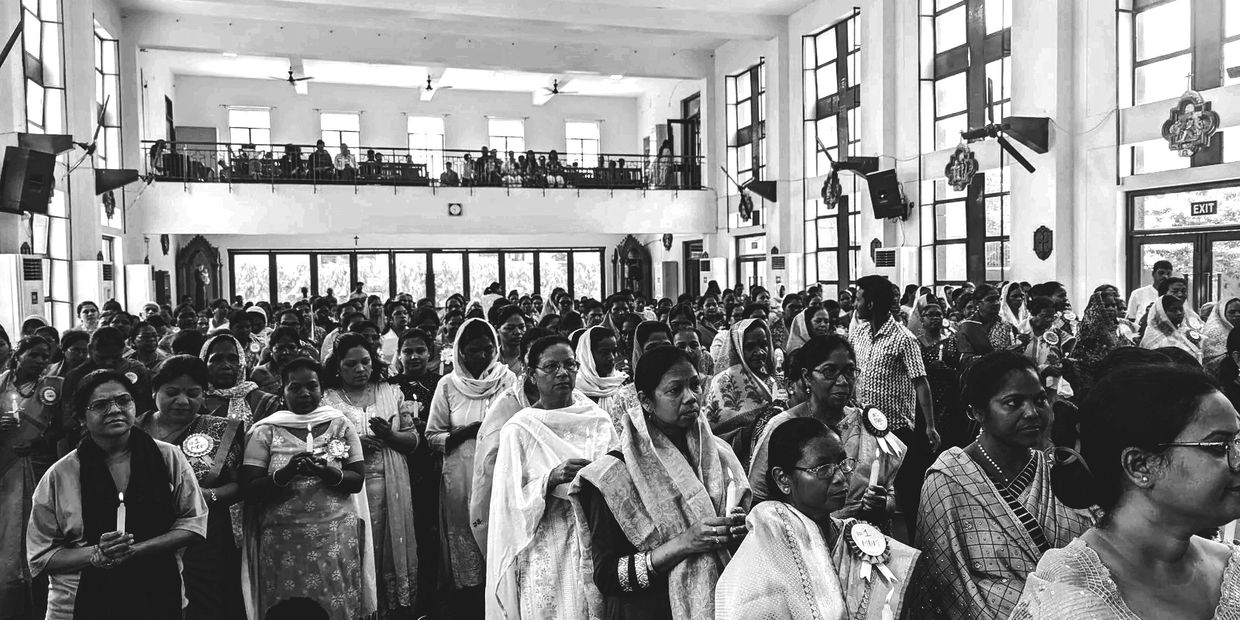 A large group of women holding candles inside a hall during a ceremonial event.