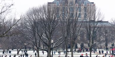 Students walking across a snowy university campus on a winter day.