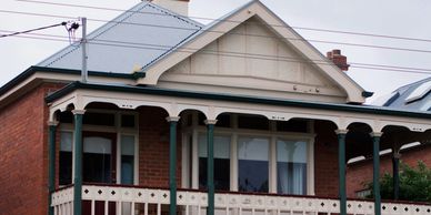 A red brick house with a veranda and ornate wooden railings.