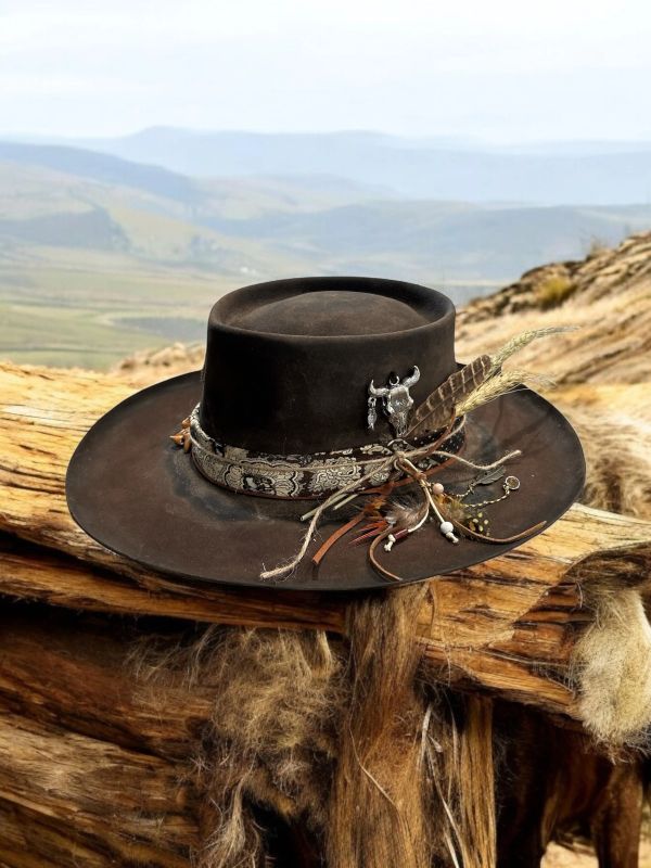 Black cowboy hat with decorative band and feathers on a wooden surface.