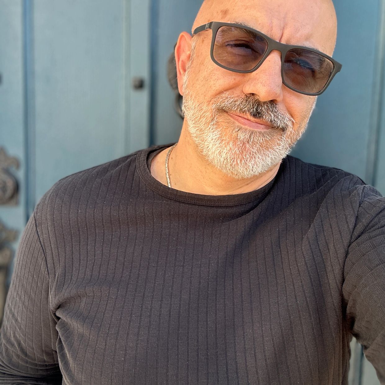 Man with sunglasses and a gray beard smiling.