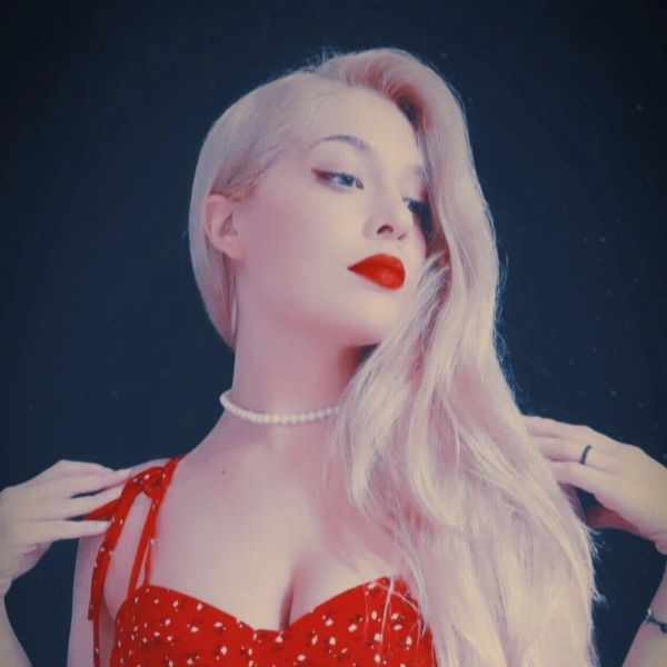 Woman with platinum blonde hair and red lipstick in a red dress.
