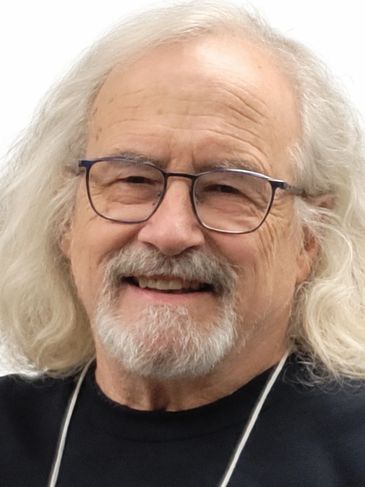 Elderly man with long white hair and glasses smiling.