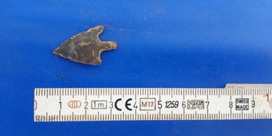 Small ancient arrowhead next to a ruler for scale.