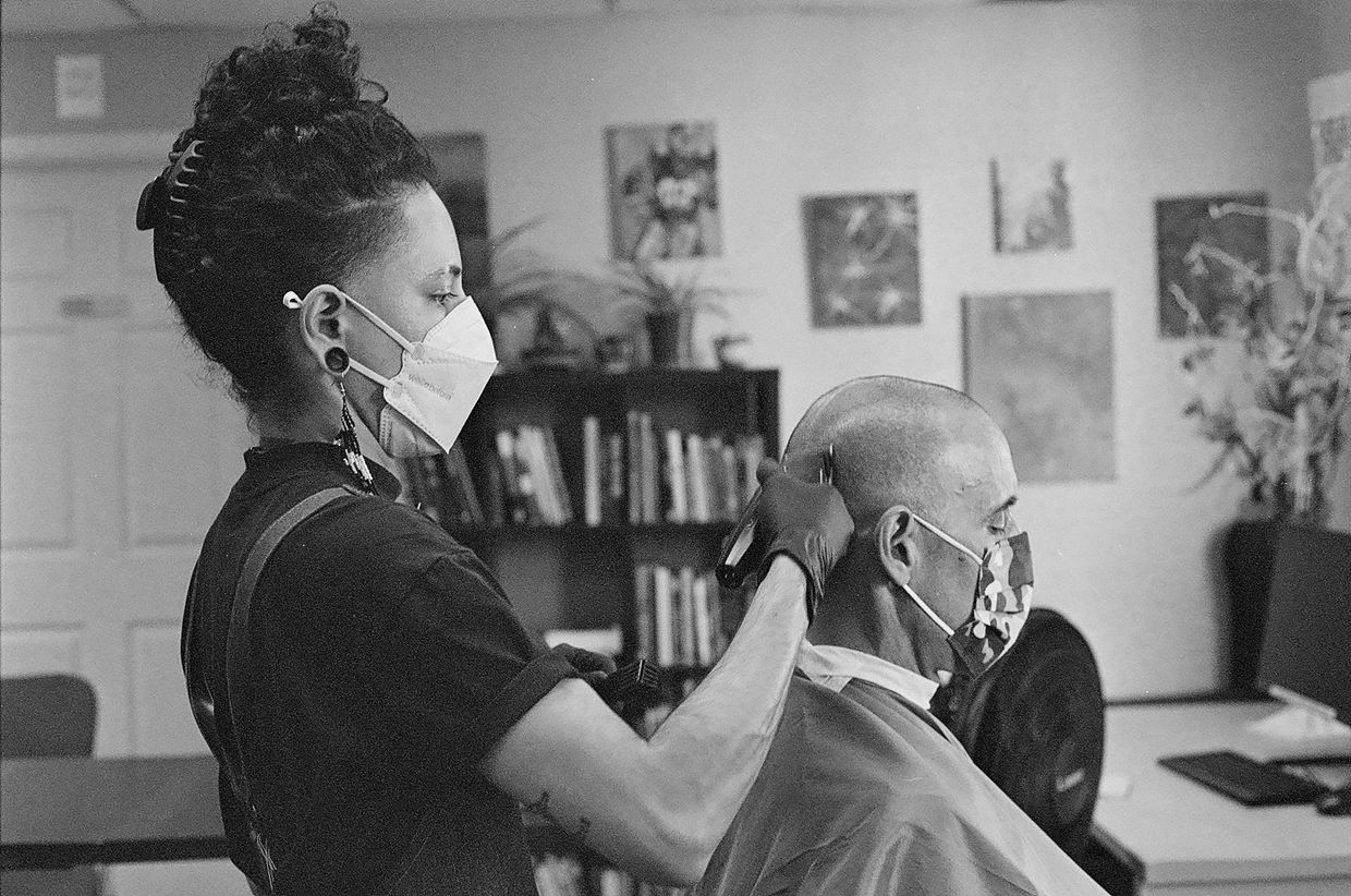Black and white photo of turtle the barber masked and working with a masked client.