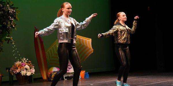 Two women dancing on stage in shiny jackets and black leggings.