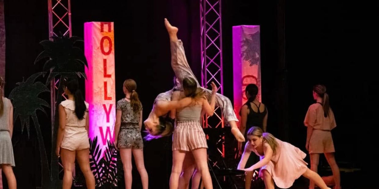 Group of dancers performing on stage under Hollywood-themed lighting.