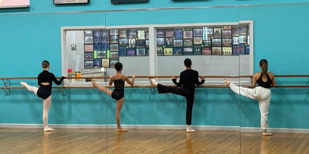 Four dancers practicing at a barre in a dance studio.