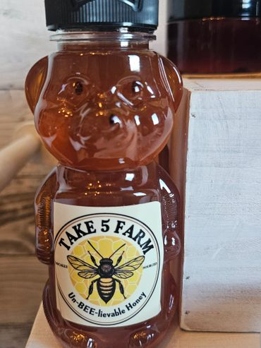 A bear-shaped bottle of honey labeled 'Take 5 Farm Un-BEE-lievable Honey.'