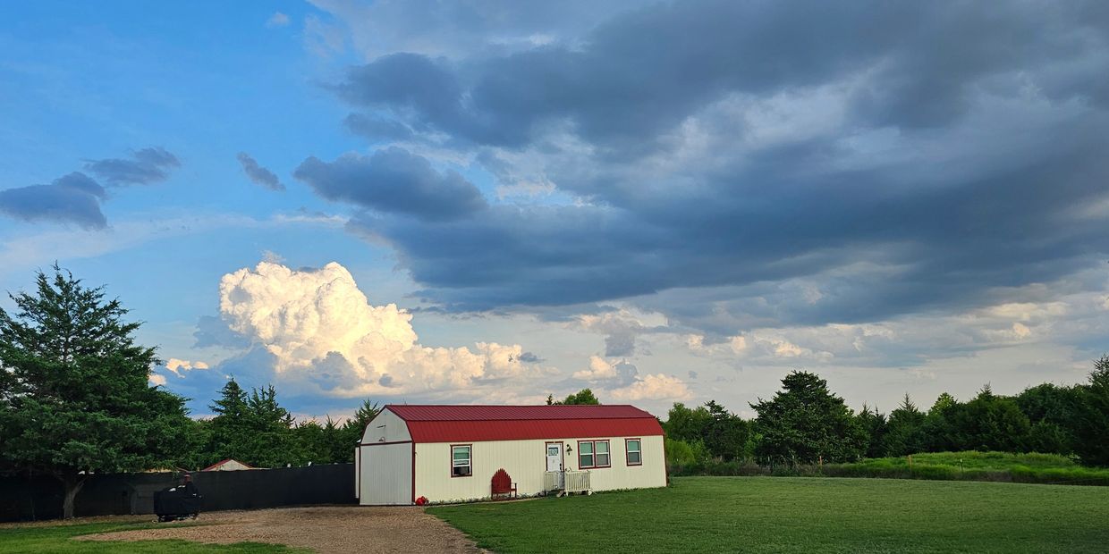 A small white house with a red roof under a dramatic cloudy sky.