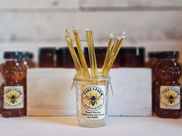 Glass jar with honey sticks and honey bear bottles in the background.