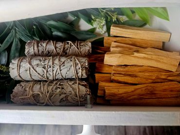 Bundles of sage and sticks of palo santo wood with green leaves.