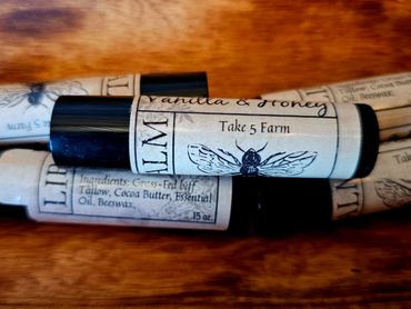 Lip balm tubes labeled Vanilla & Honey from Take 5 Farm on a wooden surface.