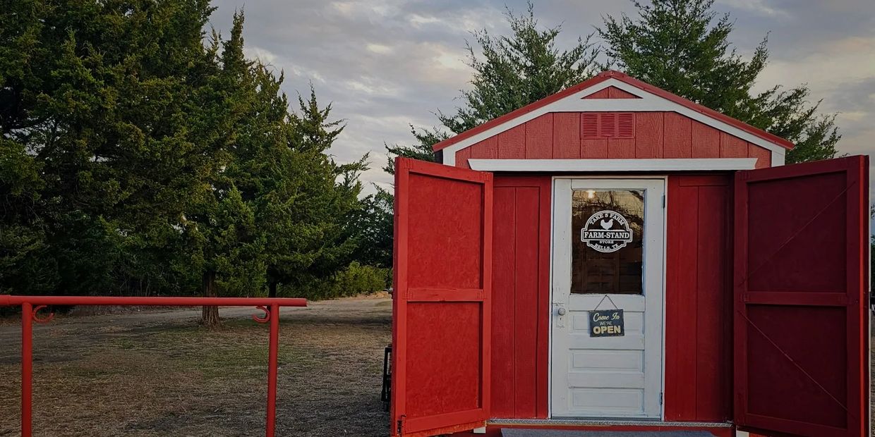 Small red farm stand with open doors in a rural setting.