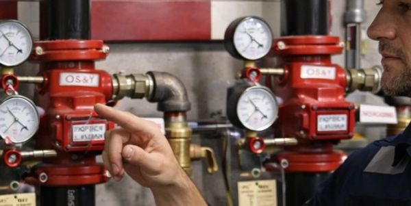Fire protection technician inspecting a fire sprinkler riser with pressure gauges and control valves